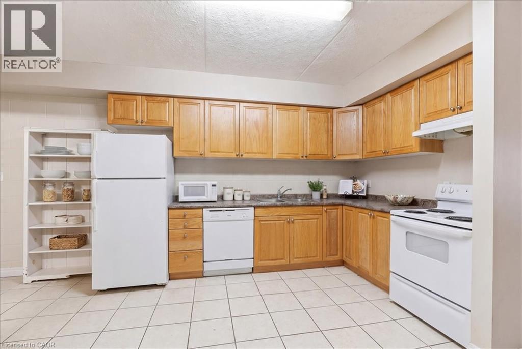 Functional kitchen featuring light wood-finish cabinetry, white appliances, and tiled flooring