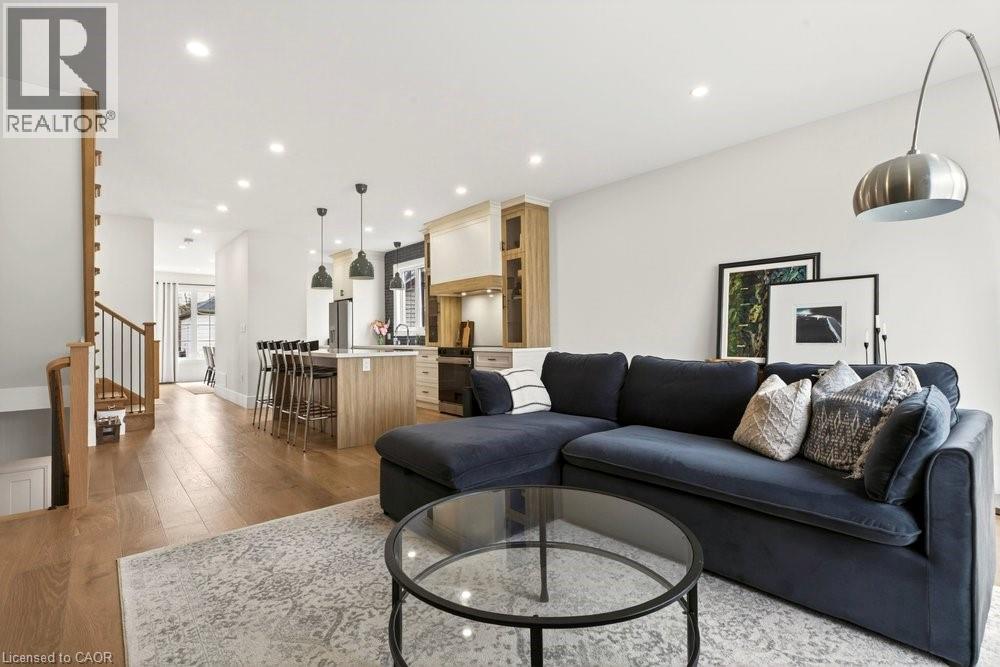 Open-concept living space featuring wood-finish flooring, recessed lighting, a kitchen island with seating, and a staircase with metal balusters