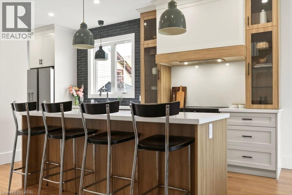 Kitchen featuring a central island with countertop seating, light wood-finish cabinetry, white upper cabinetry, and stainless steel appliances
