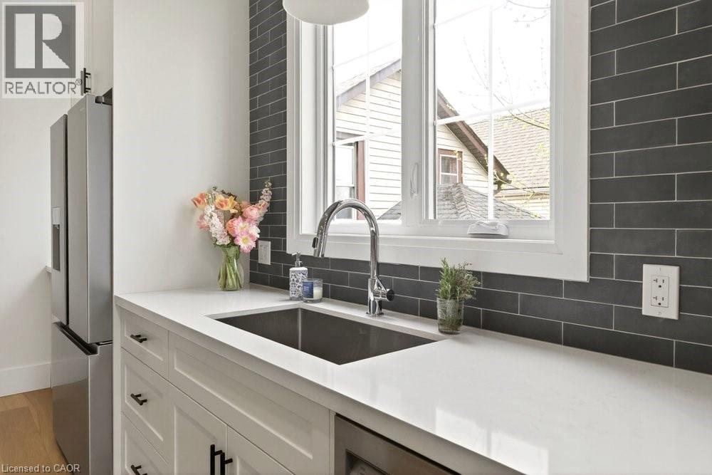 Kitchen featuring white cabinetry, a stainless steel sink with a gooseneck faucet, light-toned countertops, and a dark subway tile backsplash