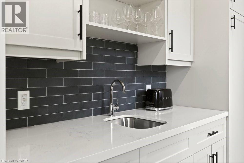 White shaker cabinetry with matte black hardware, a dark subway tile backsplash, a stainless steel undermount sink, and a chrome faucet