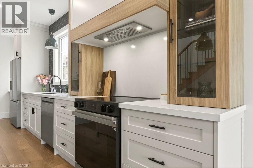 Modern kitchen featuring a stainless steel refrigerator, built-in electric range with vent hood, and a deep basin sink with a gooseneck faucet