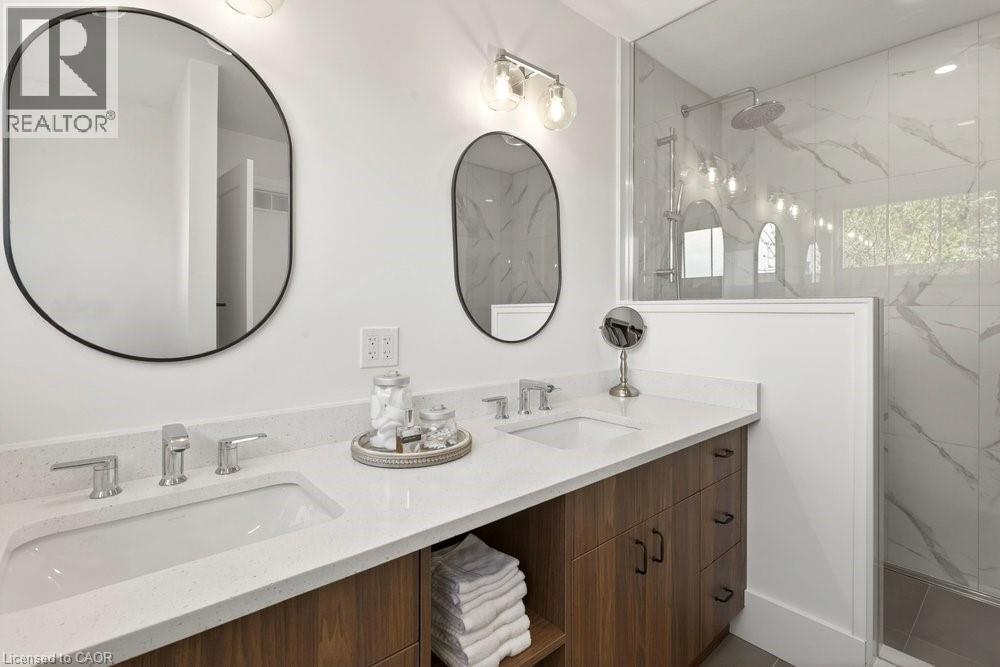 Bathroom featuring a dual-sink wood-finish vanity with stone-look countertops, chrome faucets, and two oval mirrors