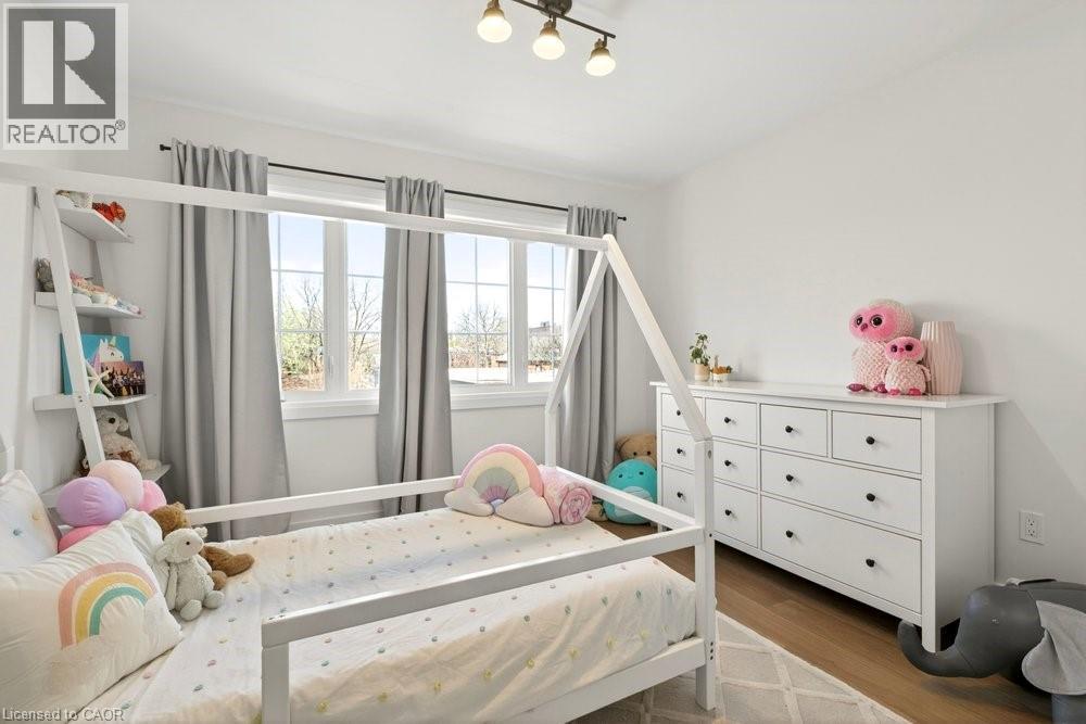 Bright room featuring multiple windows with natural light, wood-finish flooring, a white dresser with black hardware, and an overhead three-light fixture