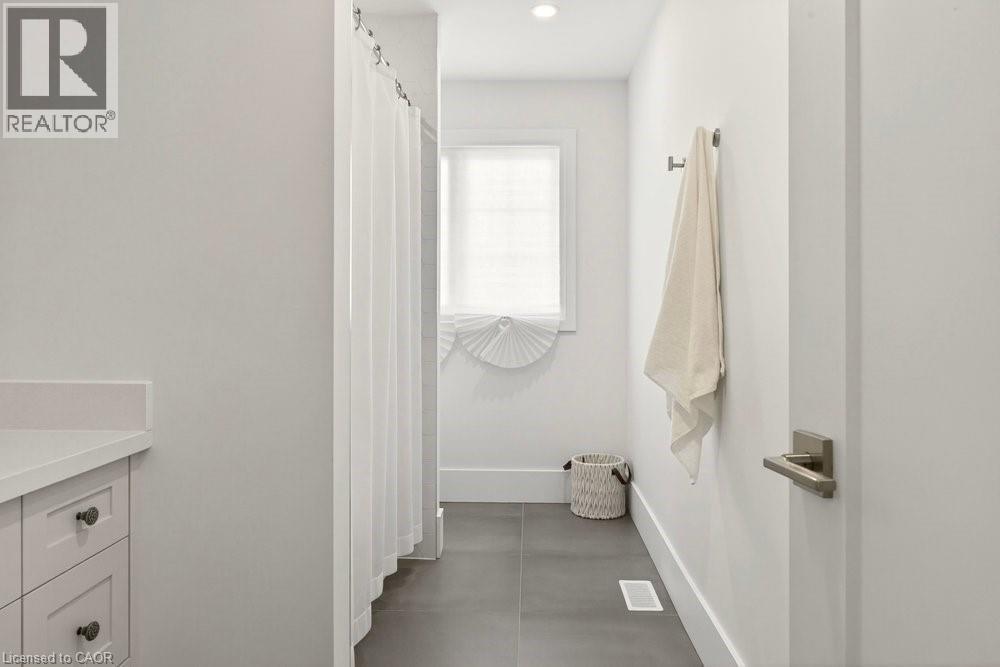 Bathroom featuring a white shower curtain, vanity with a white countertop and shaker-style cabinetry, a window with a white blind, and dark-toned floor tiles
