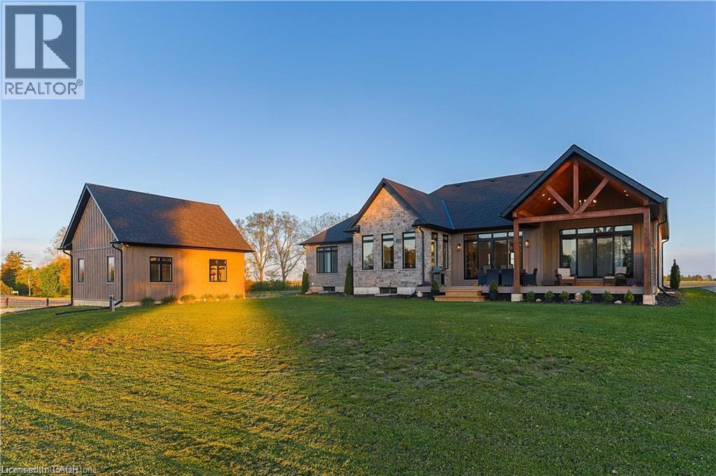 Expansive rear exterior featuring a covered patio with exposed beams, multiple sliding glass doors, a stone and siding facade, and a separate outbuilding with matching siding