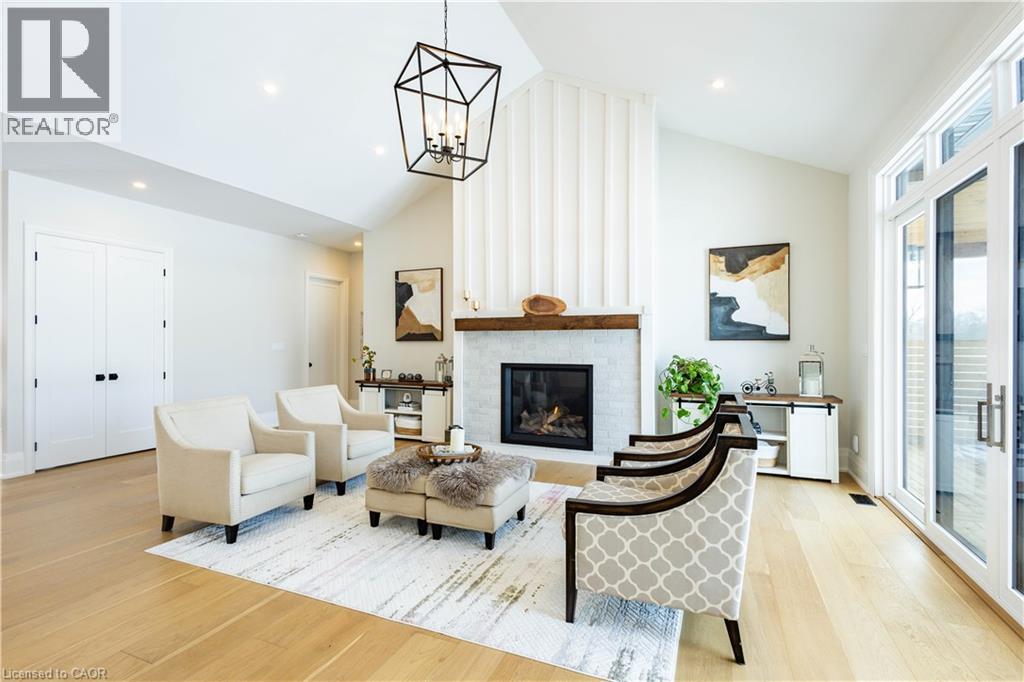 Living area featuring a vaulted ceiling with a geometric pendant light, a fireplace with a wood mantle and tile surround, light wood-finish flooring, and double glass panel doors