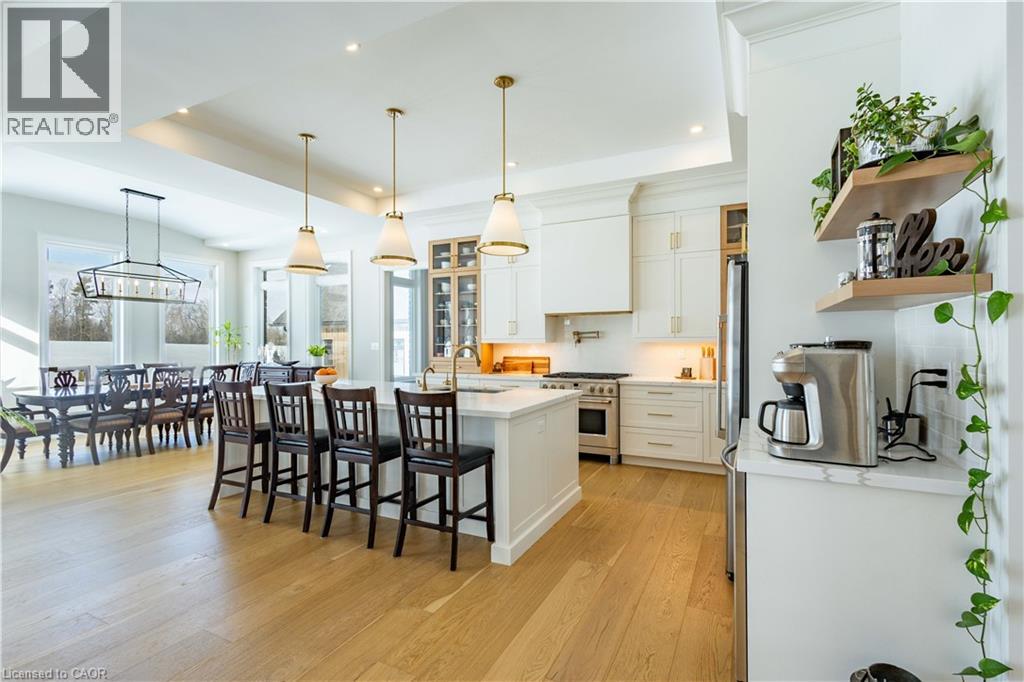 Open-concept kitchen and dining area featuring light wood-finish flooring, a kitchen island with seating, pendant lighting, white cabinetry, and stainless steel appliances
