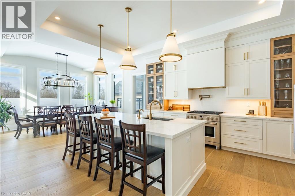 Gourmet kitchen featuring a large central island with seating, a professional-grade range, integrated range hood, white shaker cabinetry, and wood-finish flooring