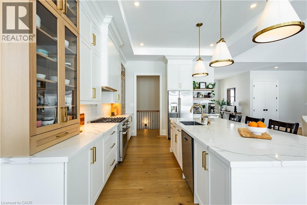 Gourmet kitchen featuring a large central island with seating, stainless steel appliances, white cabinetry with brass hardware, and wood-finish flooring