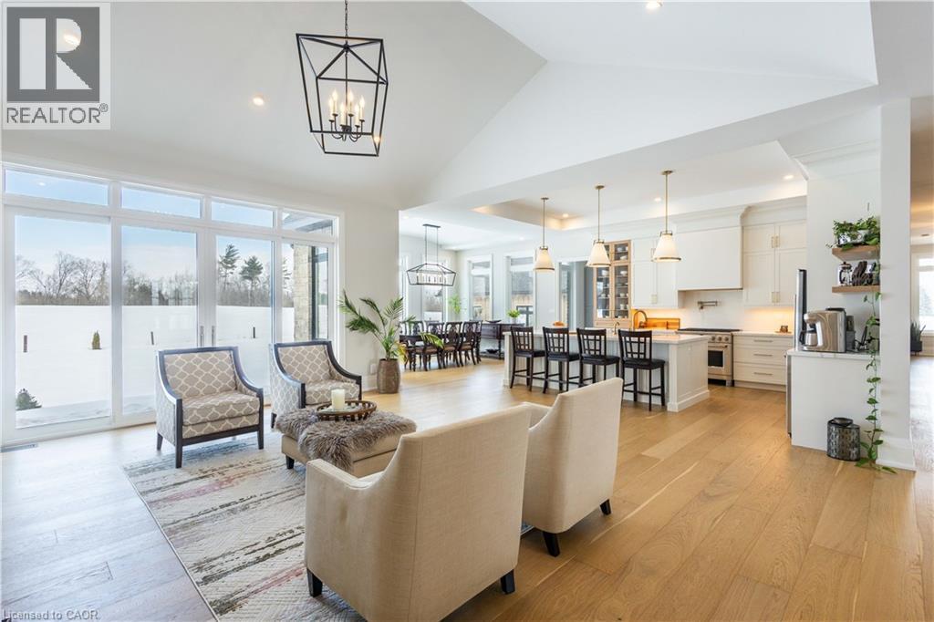 Open-concept living area featuring vaulted ceilings, wood-finish flooring, a contemporary kitchen with a large island, stainless steel appliances, and extensive window-wall patio doors