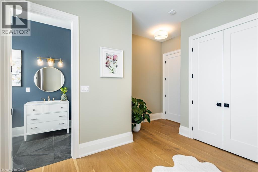 Hardwood flooring extending through a hallway with white paneled doors and a bathroom featuring a white vanity, circular mirror, and gold-finish vanity light fixtures
