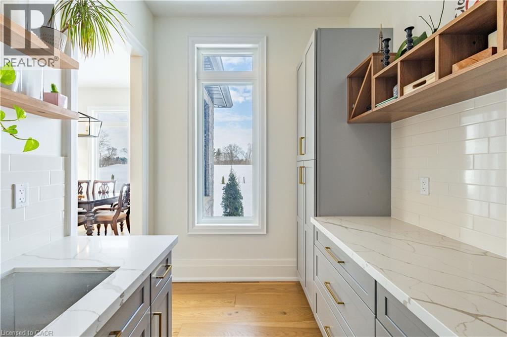 Kitchen pantry featuring extensive white countertops, wood-finish flooring, white subway tile backsplash, gray cabinetry with brass hardware, and a built-in wood-finish shelving unit