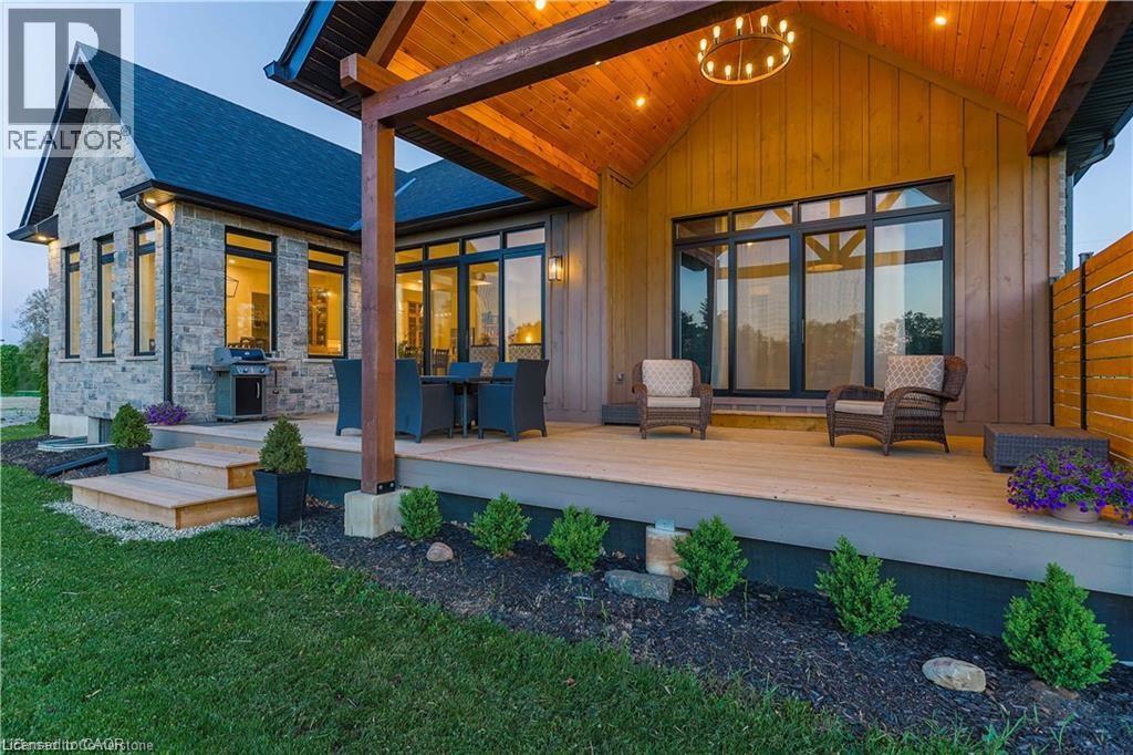 Spacious outdoor deck featuring natural wood decking, a covered patio with exposed timber beams and an overhead chandelier, multiple access points to the interior, and a stone facade on the primary st