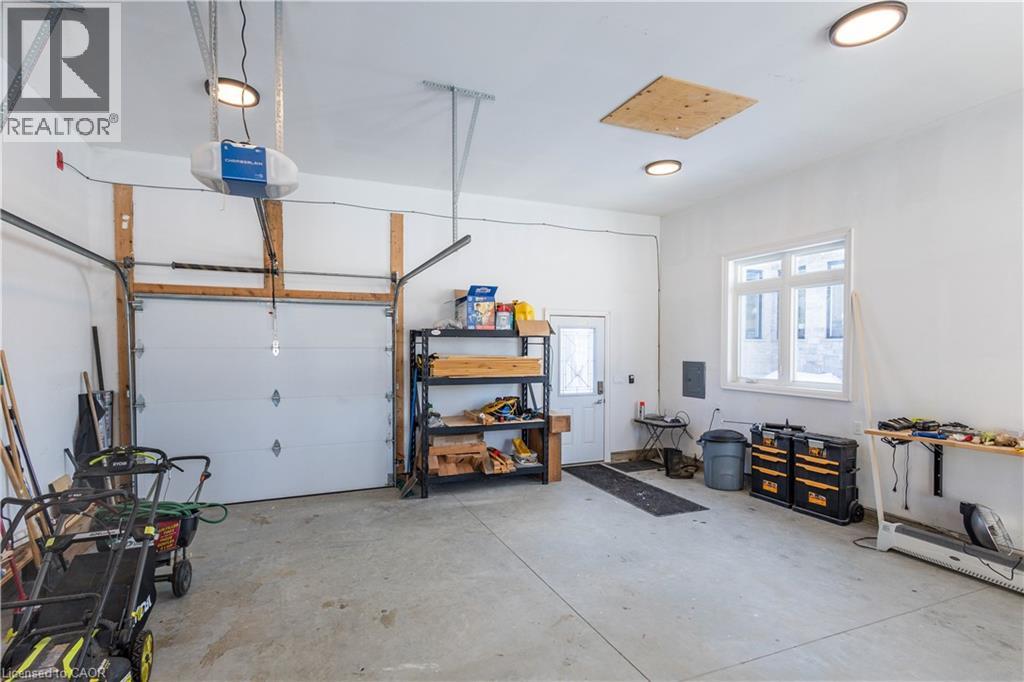 Spacious garage featuring a concrete floor, two overhead garage door openers, multiple ceiling-mounted light fixtures, a side entry door, and a multi-pane window