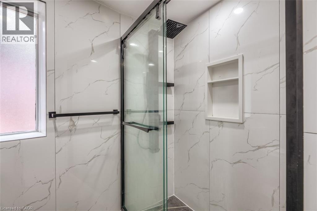 Shower enclosure featuring a frameless glass door, black matte fixtures, a rain showerhead, a built-in shower niche, and large format marble-look tile walls