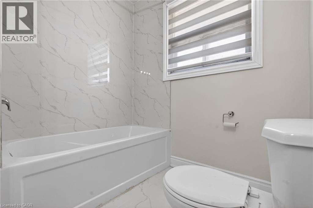 Bathroom featuring a white soaking tub with polished chrome fixtures, white marbled tile surround, and a white toilet