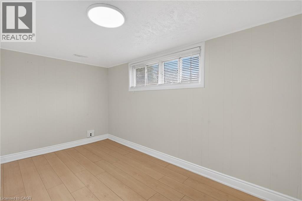 Room featuring wood-finish flooring, a window with horizontal blinds, light-toned wall paneling, white baseboards, and a flush-mount ceiling light fixture