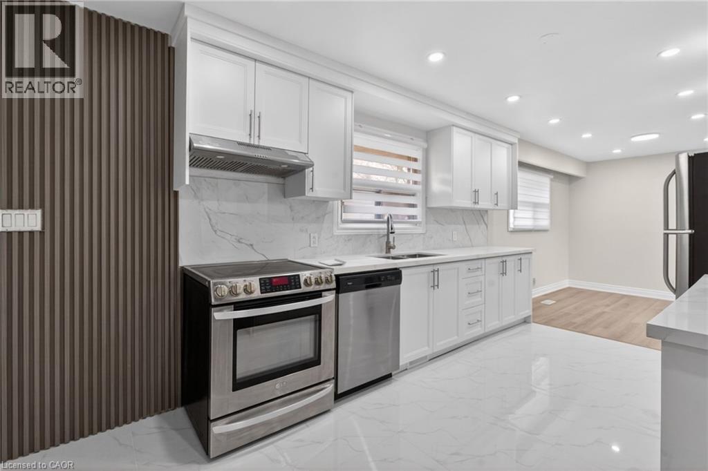 Contemporary kitchen featuring white cabinetry, stainless steel appliances, a white stone-look backsplash, and integrated ceiling lighting
