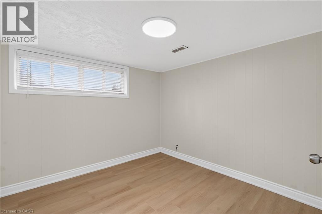 Room featuring wood-finish flooring, a rectangular window with blinds, and a flush-mount ceiling light