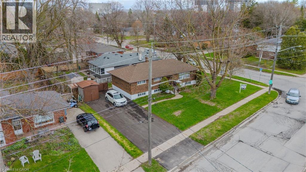 Brown brick exterior featuring a brown shingle roof, established front lawn, paved driveway, and detached storage sheds