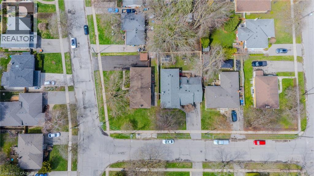 Aerial view of a residential corner lot property featuring an asphalt driveway and a detached dwelling with a dark shingle roof