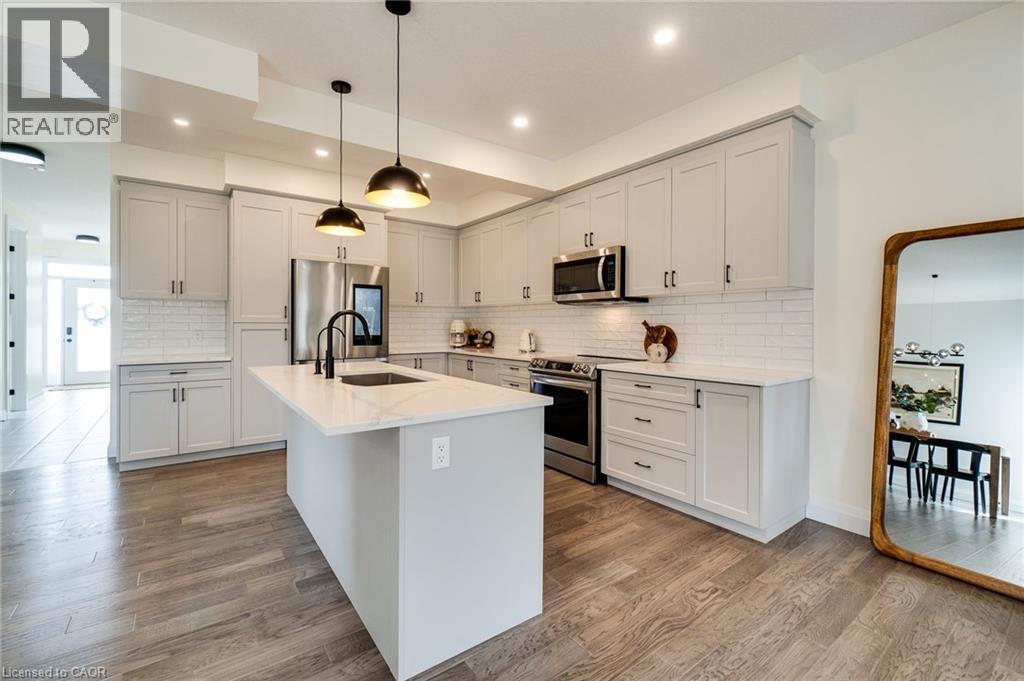 Modern kitchen featuring white shaker cabinetry, stainless steel appliances, a center island with sink, subway tile backsplash, and wood-finish flooring