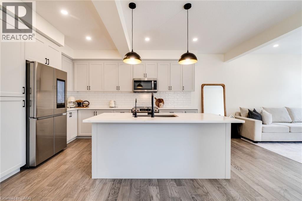 Kitchen featuring a central island with a sink and matte black faucet, stainless steel appliances, light cabinetry, and white subway tile backsplash