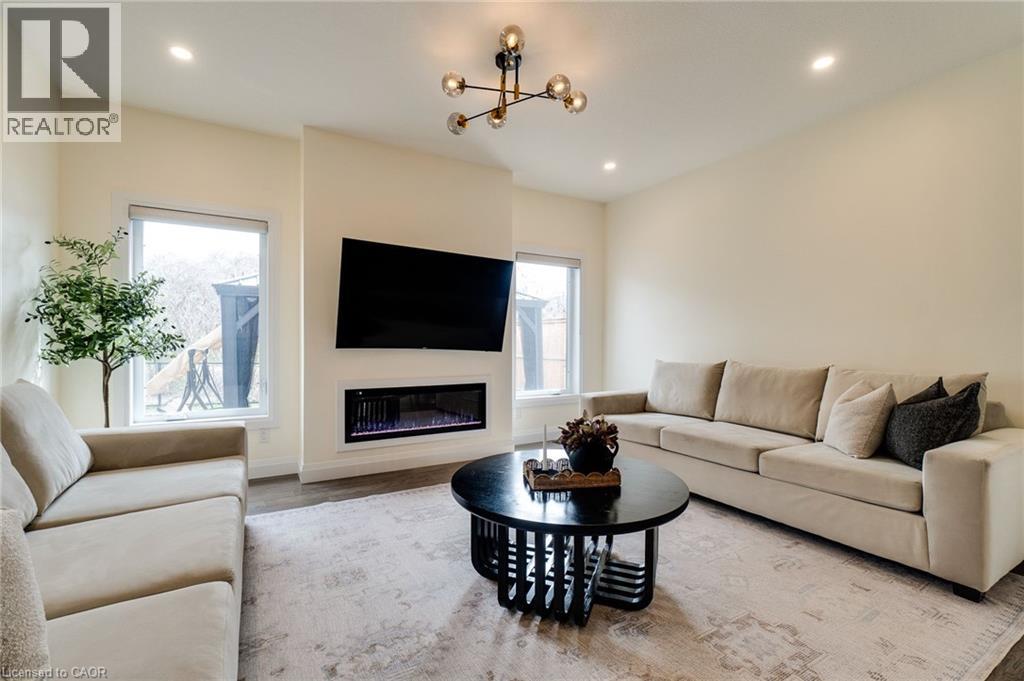 Living area featuring a wall-mounted electric fireplace, recessed lighting, two large windows, wood-finish flooring, and a modern chandelier