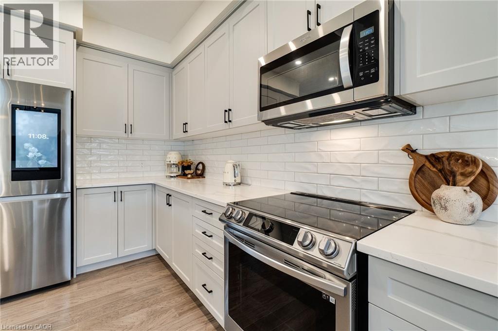 Modern kitchen featuring light-toned cabinetry with dark hardware, stainless steel appliances, and quartz countertops