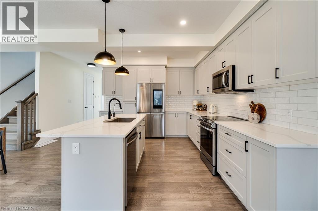 Modern kitchen featuring light cabinetry, stainless steel appliances, a white subway tile backsplash, and a large island with a sink and breakfast bar
