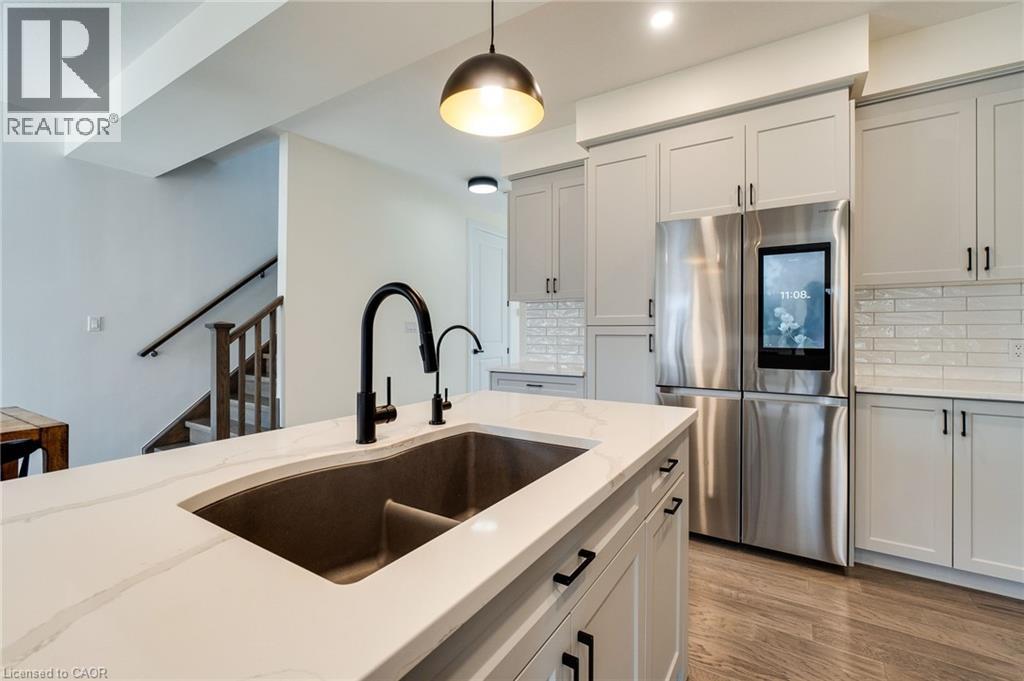 Kitchen island featuring a dual-basin sink with a matte black faucet, quartz countertop, and light-toned cabinetry with dark hardware