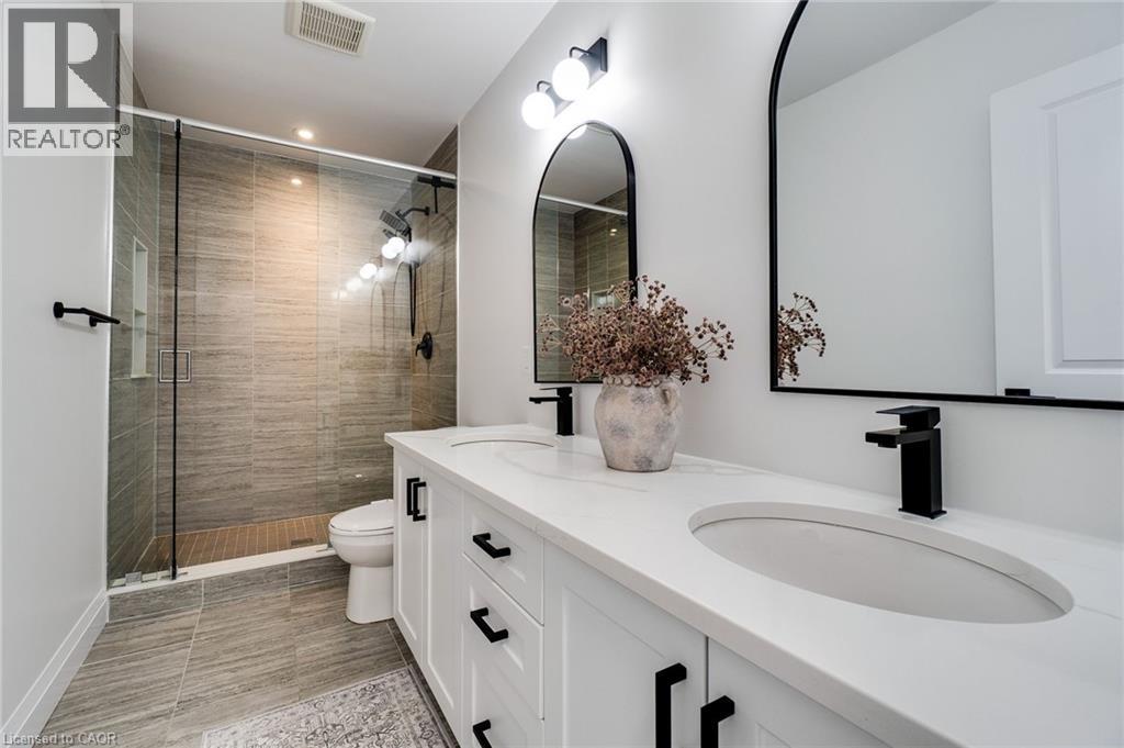 Modern bathroom featuring a dual vanity with white cabinetry, matte black hardware, and two arched mirrors