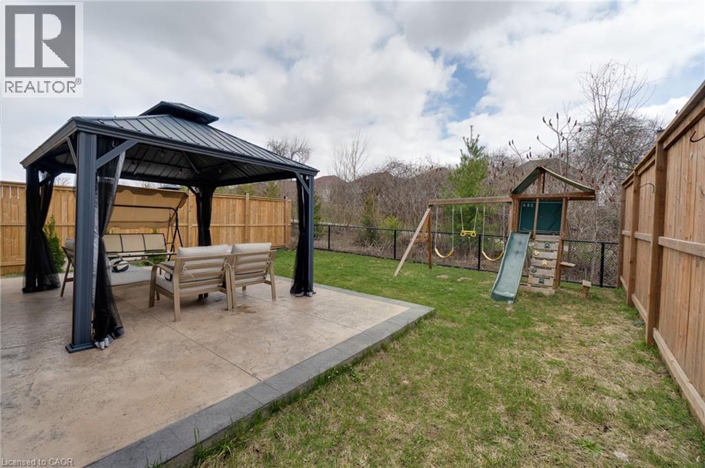 Expansive backyard featuring a stamped concrete patio, a dark-framed gazebo with privacy curtains, a wooden privacy fence, a black metal fence, and a swing set with slide