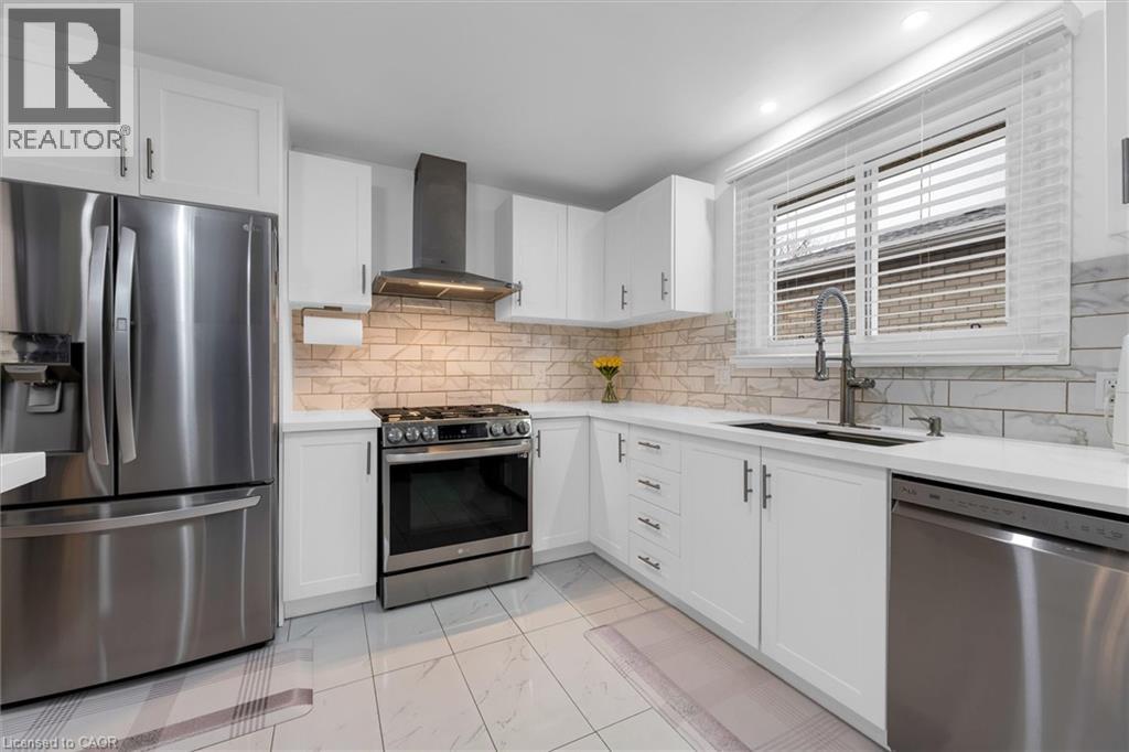 Kitchen with stainless steel appliances, light marble finish floors, white cabinets, and tasteful backsplash