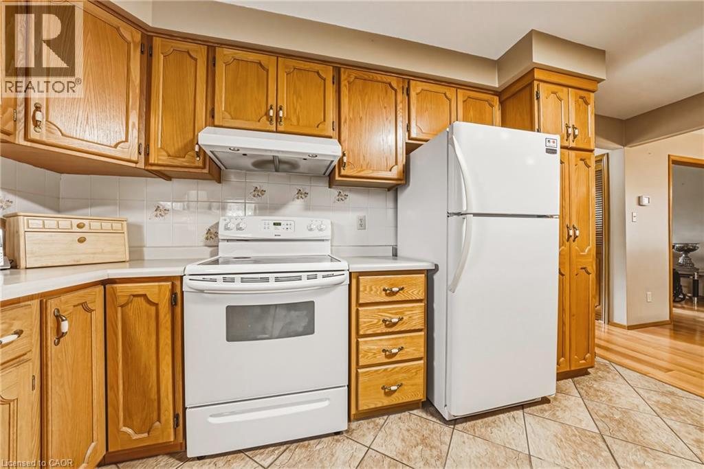 Kitchen featuring wood cabinetry, white appliances, white tile backsplash, and light-colored countertops