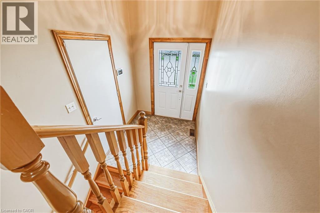 Wood-finish staircase with natural wood banister, white paneled door with wood trim, white entrance door with decorative glass inserts, and tiled flooring