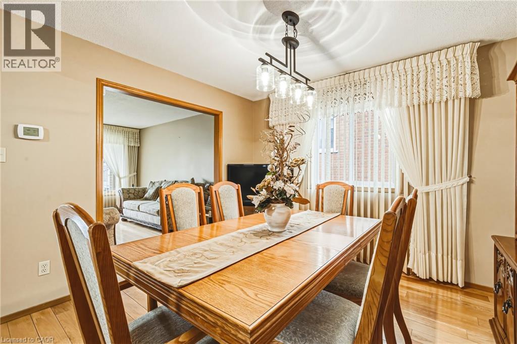 Dining area featuring wood-finish flooring, a contemporary ceiling light fixture, a window with vertical blinds and fabric drapes, and a wide cased opening to an additional room