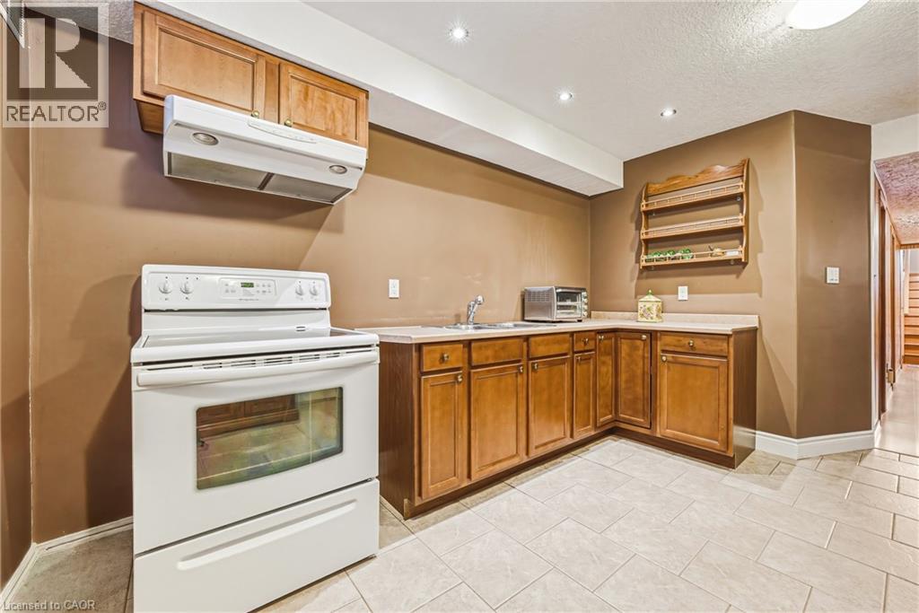 Kitchenette featuring light wood-finish cabinetry, white electric range with overhead exhaust, light-toned countertop, and tiled flooring