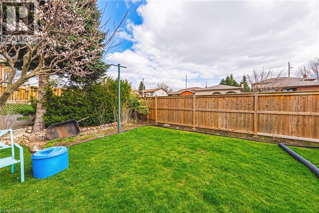 Fenced backyard featuring a manicured lawn, established perimeter landscaping, and a mature tree