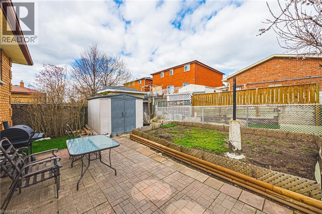 Paved patio area featuring brick-patterned pavers, a garden bed with a wooden border, and a functional storage shed