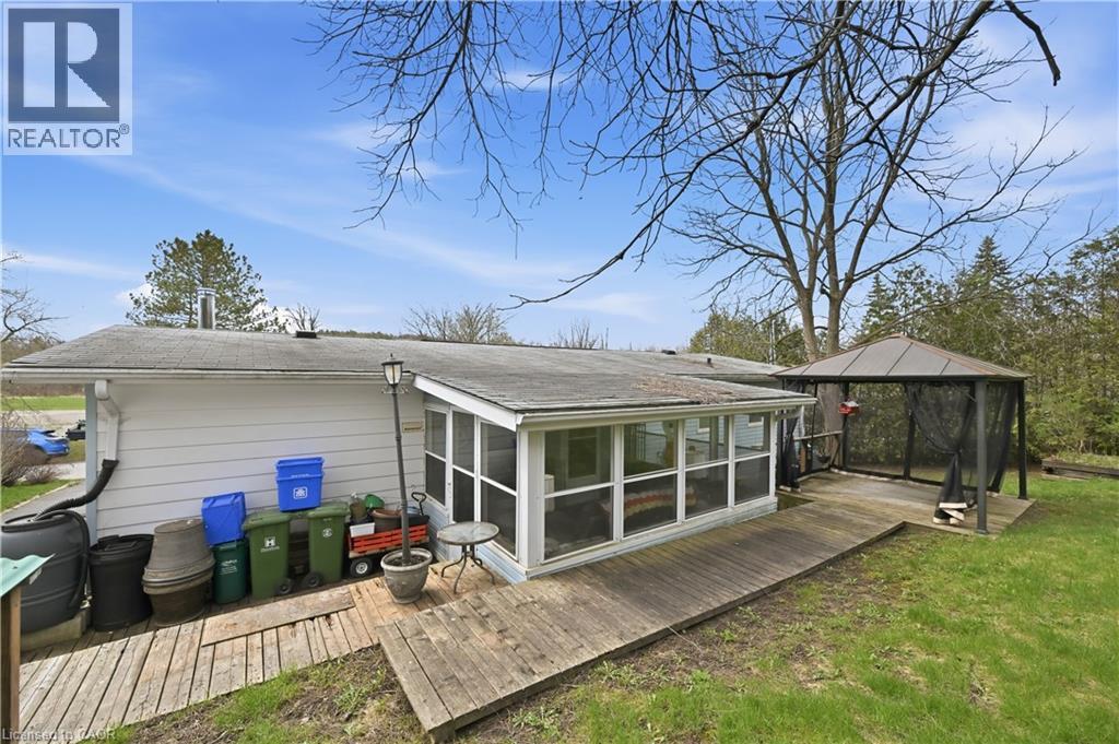 Exterior featuring a screened-in porch with multiple windows, a wood deck, and a detached gazebo with netting