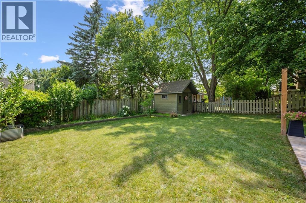 Expansive green lawn featuring a detached shed with a gable roof, mature trees, wood privacy fencing, and a white picket fence