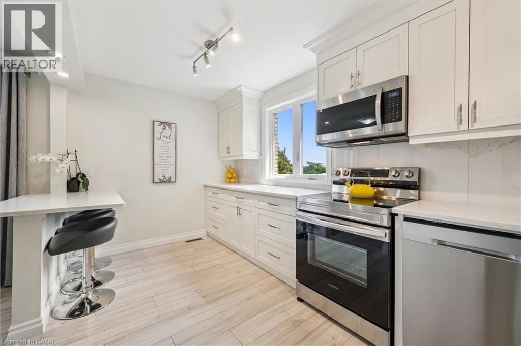 Bright kitchen featuring stainless steel appliances, white cabinetry, a built-in breakfast bar, recessed lighting, and wood-finish flooring
