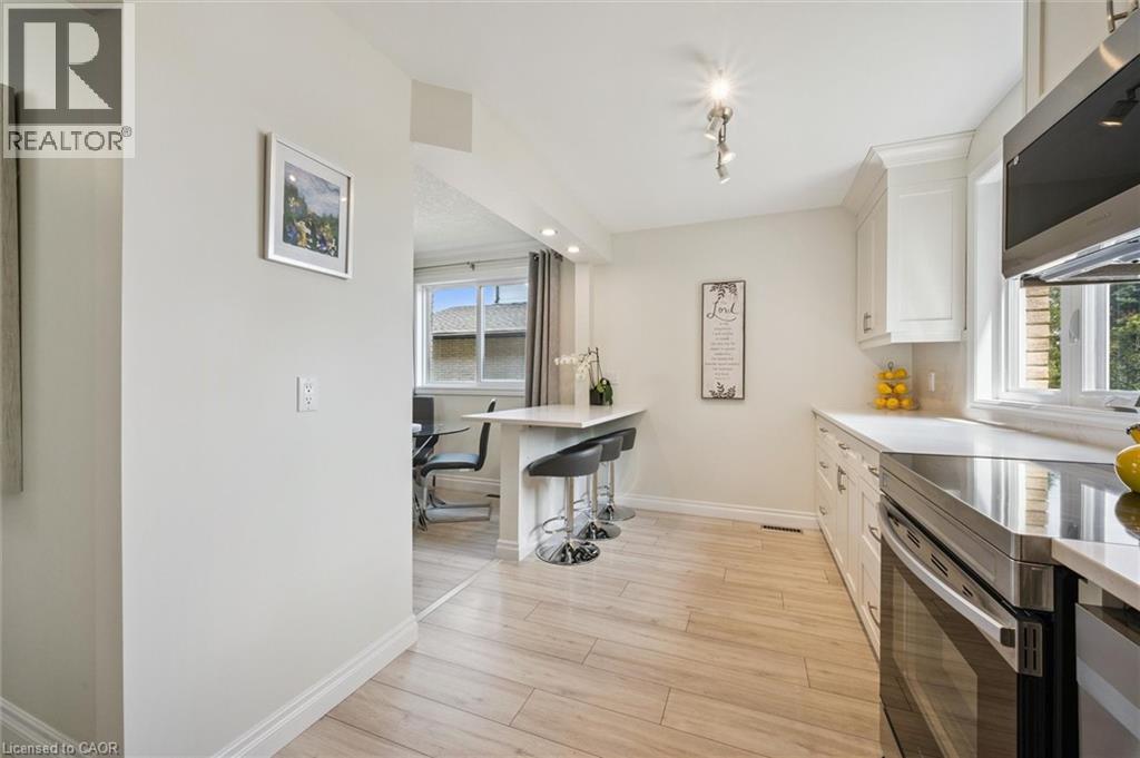 Kitchen featuring wood-finish flooring, white cabinetry, integrated stainless steel appliances, and a breakfast bar with seating