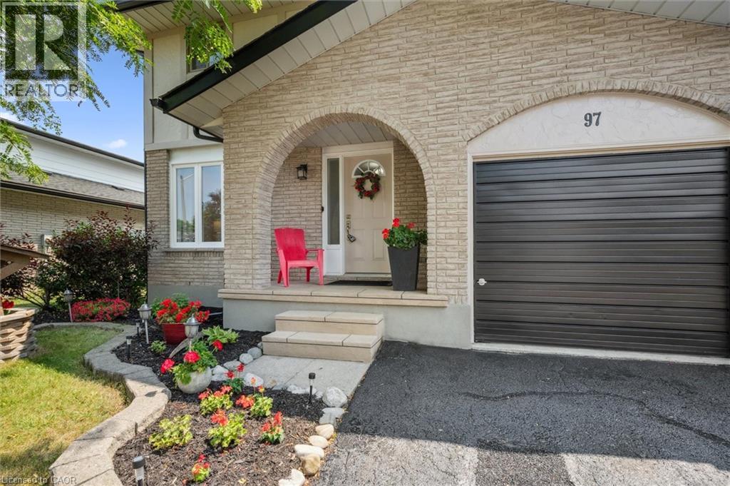 Brick facade entryway with an arched portico, featuring a dark panel garage door, white front door, and manicured front landscaping
