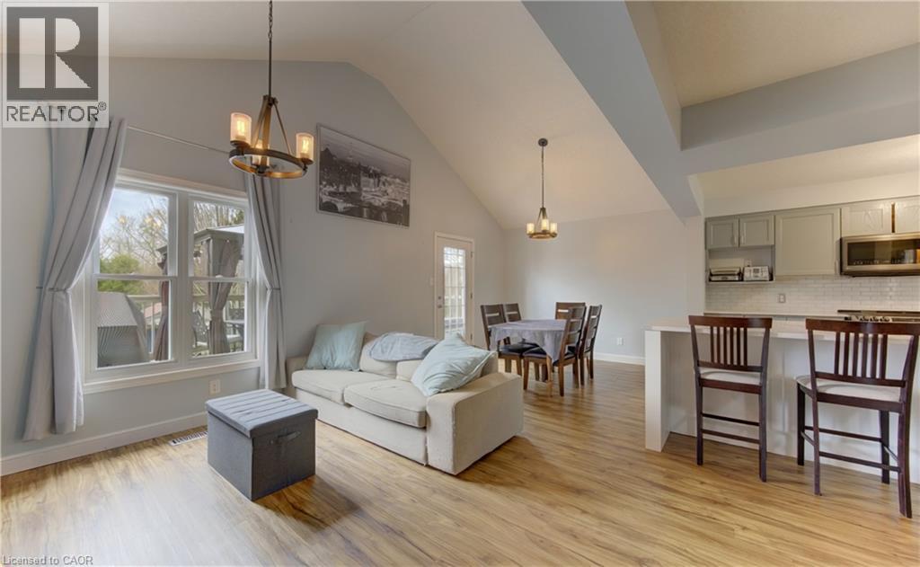 Open-concept living space with vaulted ceilings, wood-finish flooring, a kitchen island with seating, pendant lighting, and a dining area with direct outdoor access