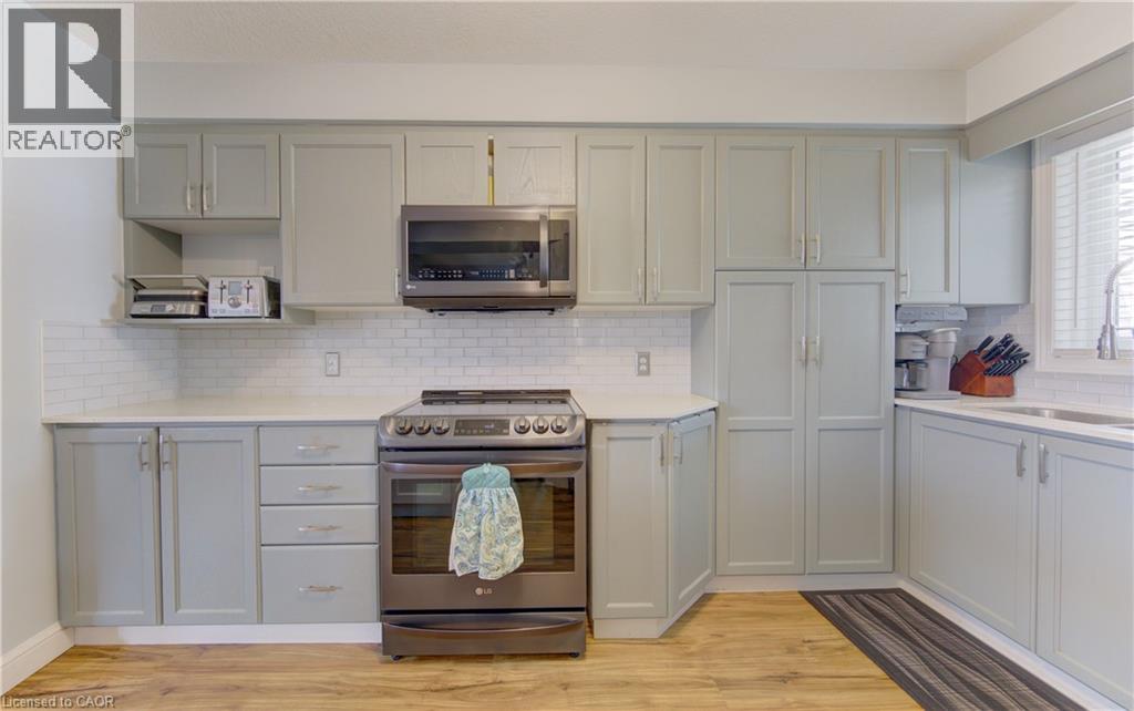 Kitchen featuring light gray cabinetry, stainless steel appliances, a white subway tile backsplash, light countertops, and wood-finish flooring