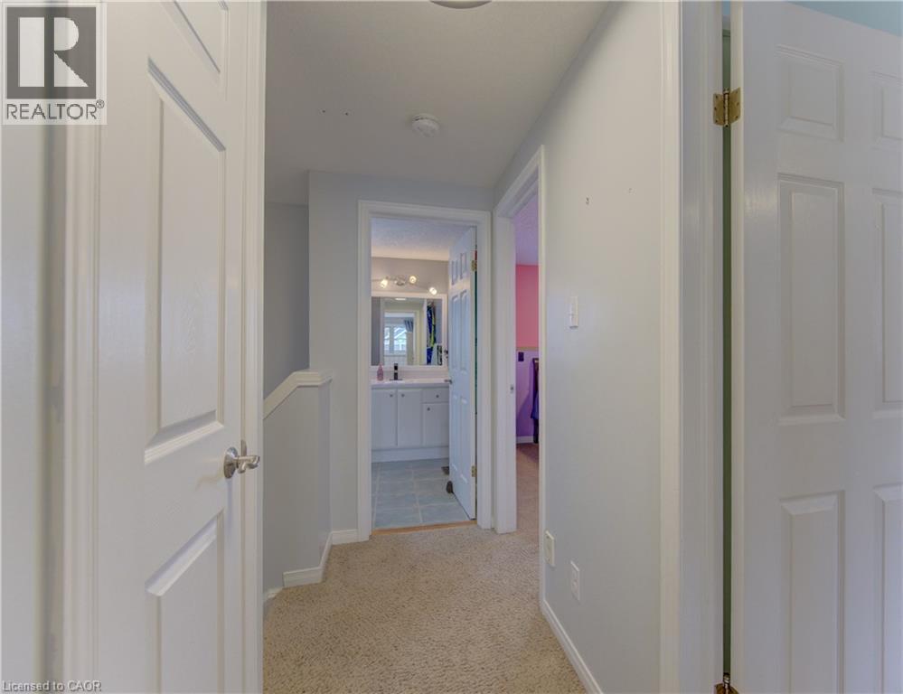 Carpeted hallway with white interior doors, leading to a bathroom featuring a white vanity with a mirror and multi-bulb light fixture