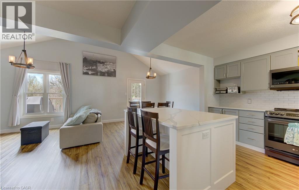 Open-concept living space featuring wood-finish flooring, vaulted ceilings with exposed beams, and a modern kitchen